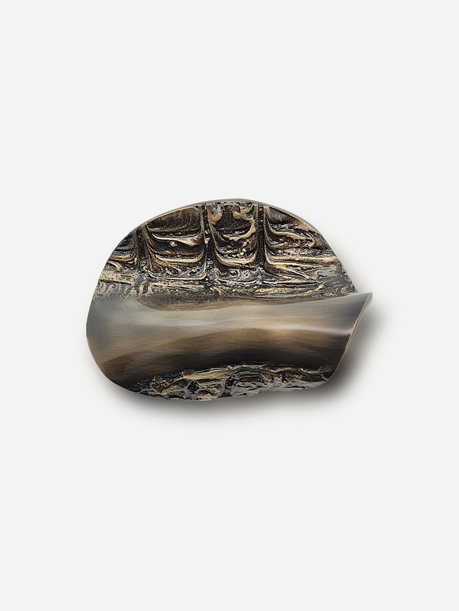 A bronze-colored metal cabinet pull with a sculpted design, featuring hand-folded brass accents for cabinets and drawers